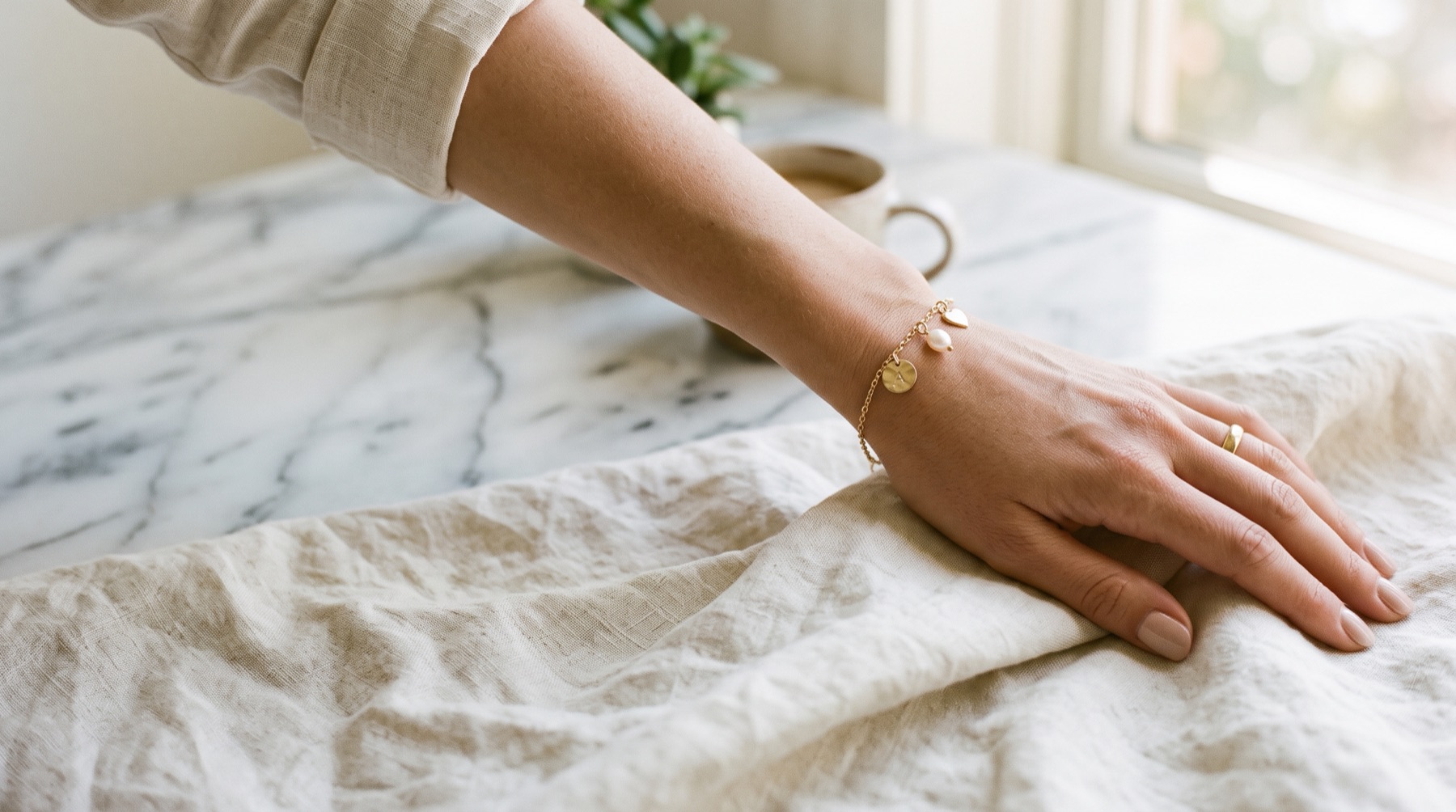 A wrist on pale linen wearing a gold charm bracelet